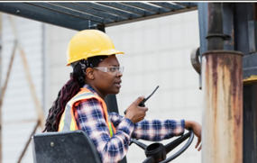 Woman in hard hat speaking into a 2-way radio.